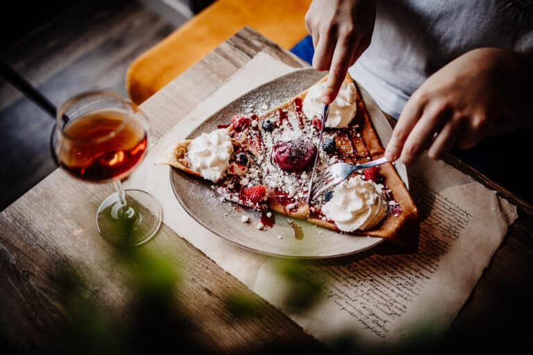 un verre de rhum arrangé sur la table d'une crêperie, avec quelqu'un qui est en train de découper une crêpe garnie